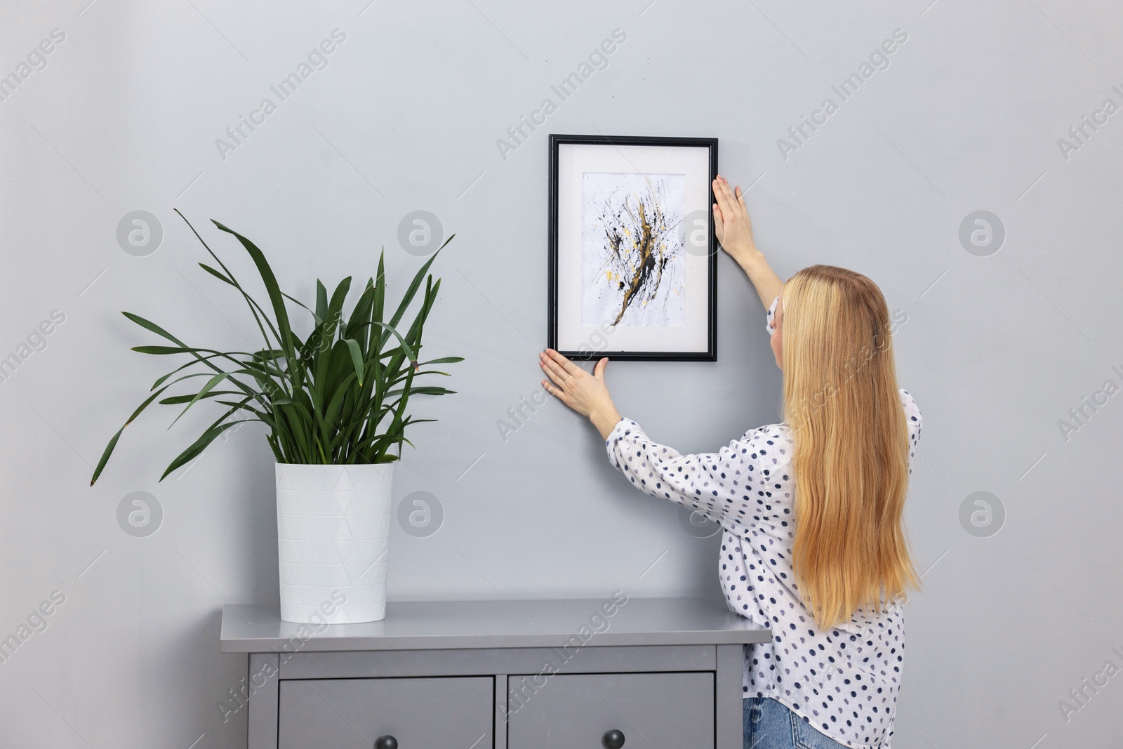 Photo of Female decorator hanging abstract picture indoors, back view