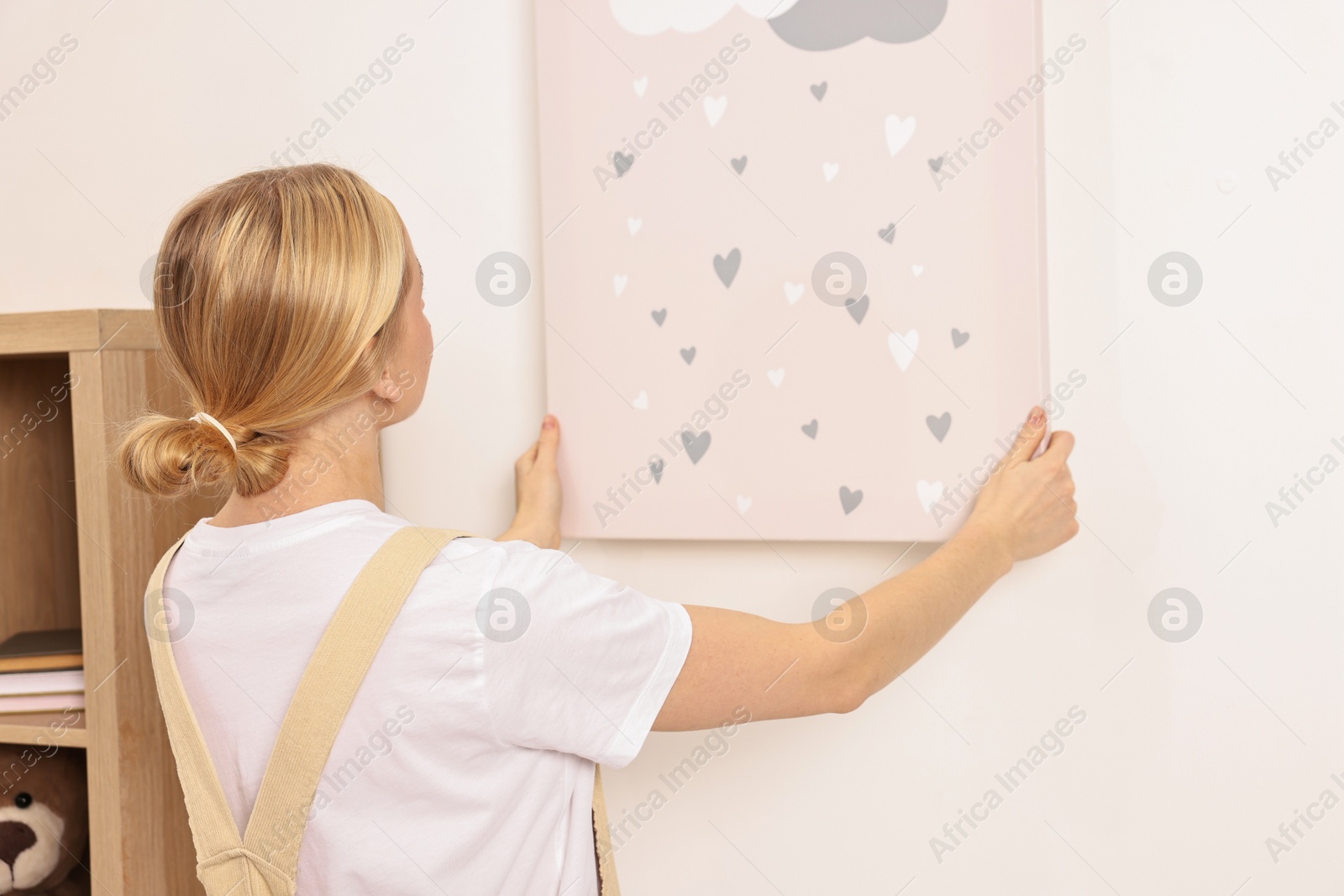 Photo of Female decorator hanging picture on wall indoors, back view