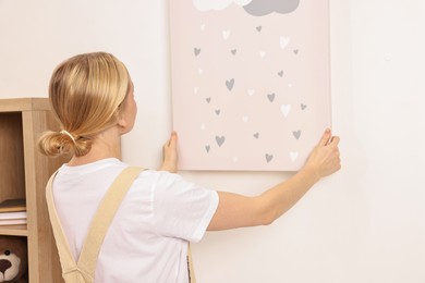 Photo of Female decorator hanging picture on wall indoors, back view