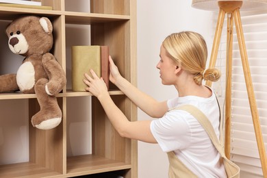 Female decorator arranging books onto shelving unit in child's room