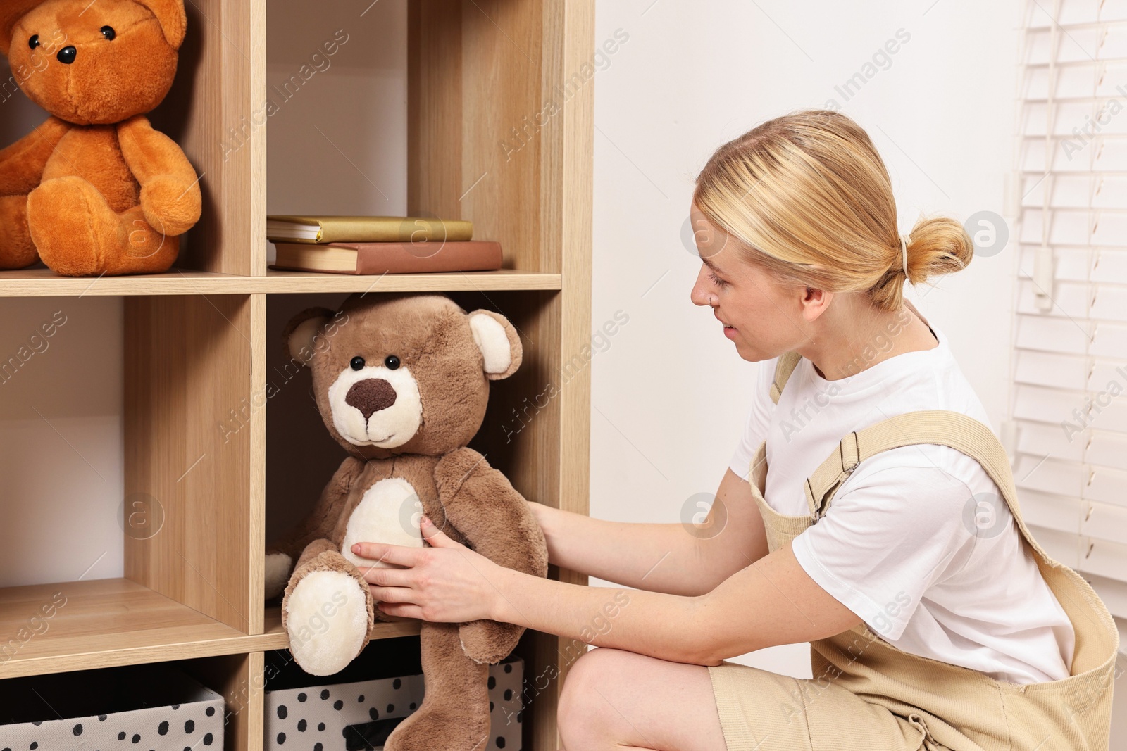 Photo of Female decorator arranging toy onto shelving unit in child's room