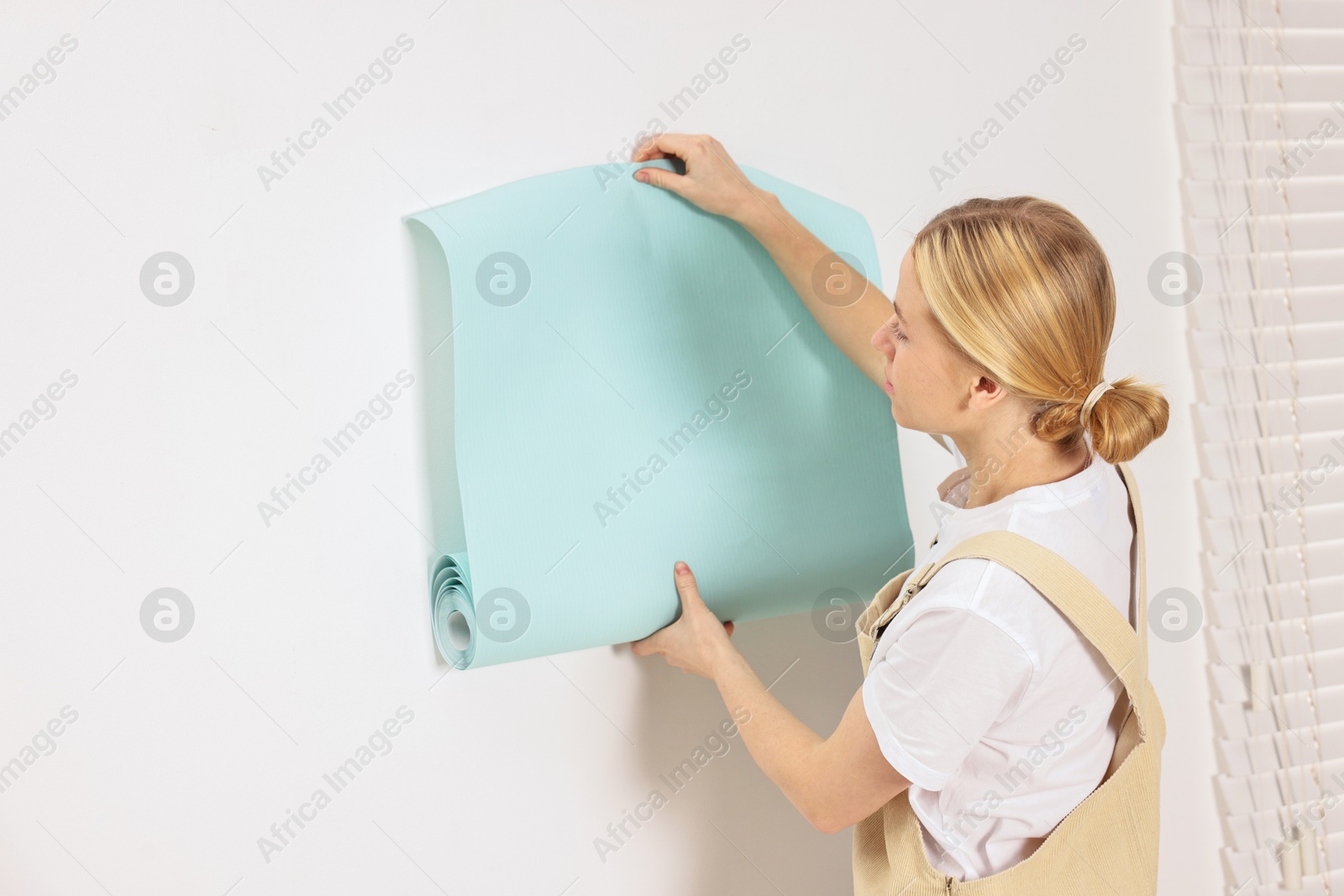 Photo of Female worker hanging turquoise wallpaper onto wall indoors. Space for text