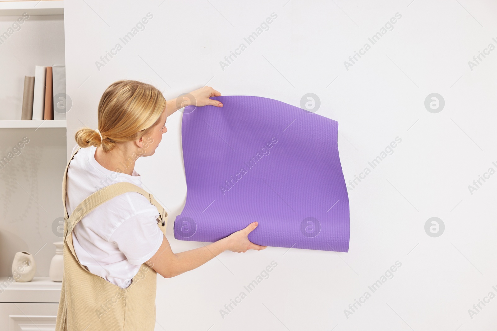 Photo of Female worker hanging violet wallpaper onto wall indoors