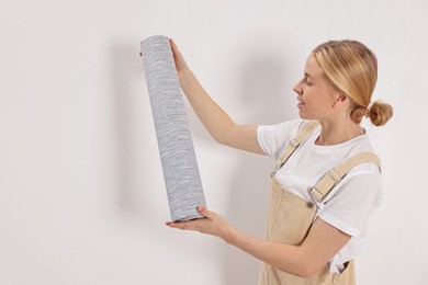 Smiling worker with roll of grey wallpaper indoors, space for text