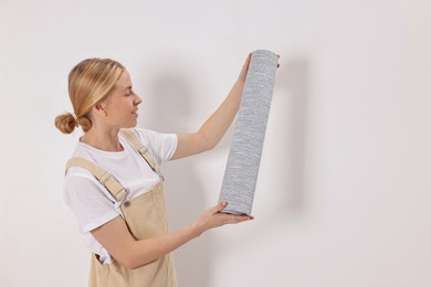 Smiling worker with roll of grey wallpaper indoors, space for text