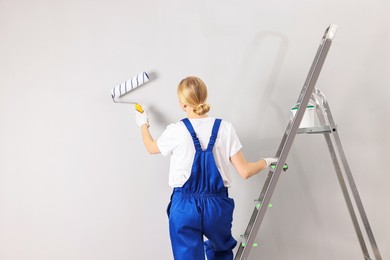 Female worker painting wall with roller indoors, back view. Space for text