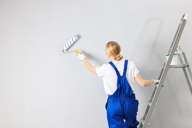 Photo of Female worker painting wall with roller indoors, back view. Space for text