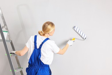 Photo of Female worker painting wall with roller indoors, back view. Space for text