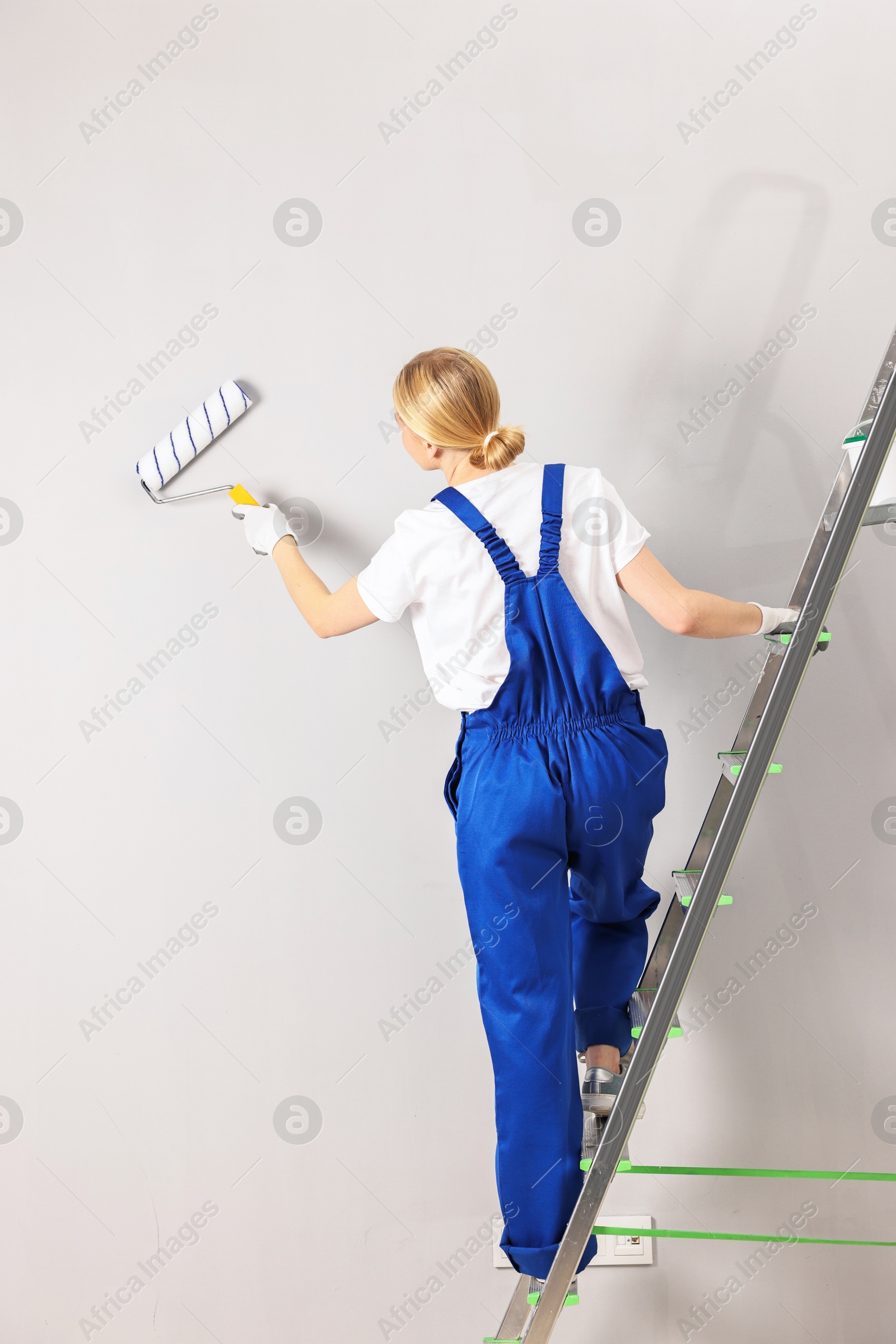 Photo of Female worker painting wall with roller indoors, back view