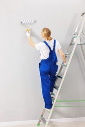 Female worker painting wall with roller indoors, back view