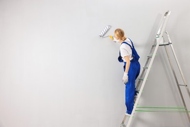 Female worker painting wall with roller indoors, back view. Space for text