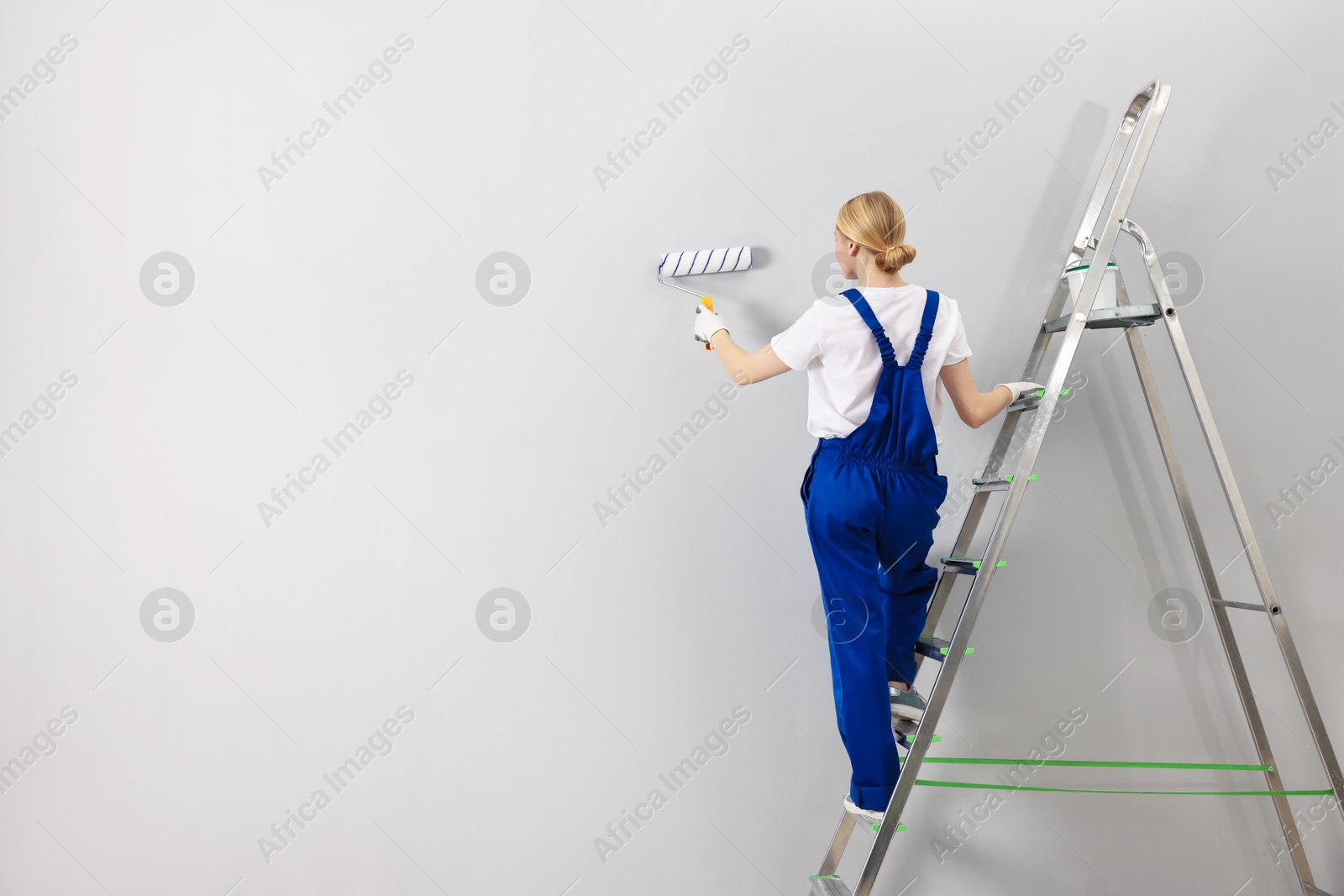 Photo of Female worker painting wall with roller indoors, back view. Space for text