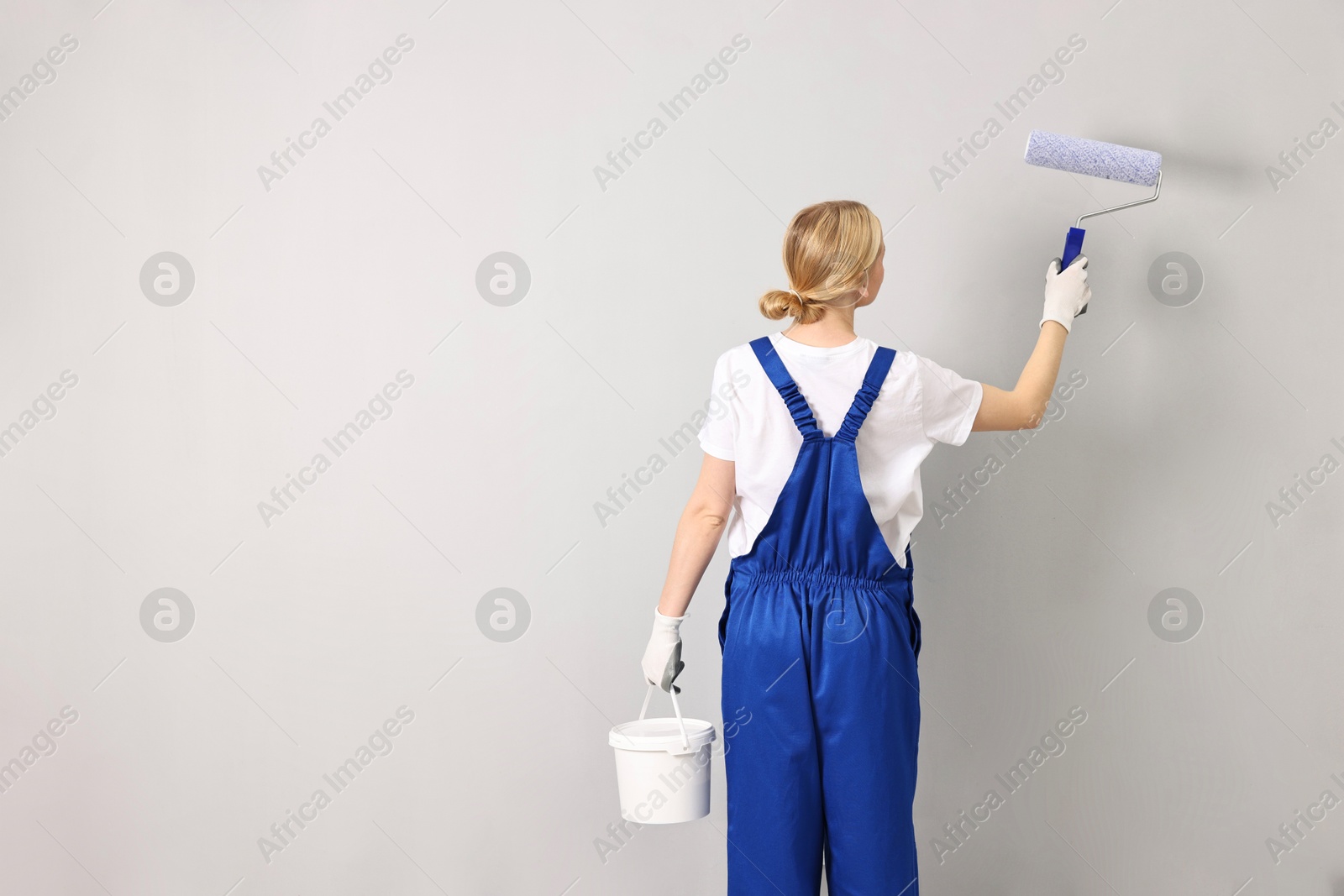 Photo of Female worker painting wall with roller indoors, back view. Space for text