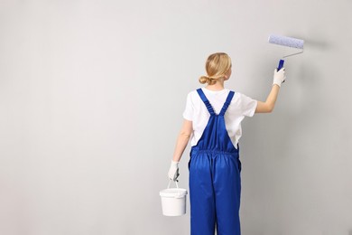 Female worker painting wall with roller indoors, back view. Space for text