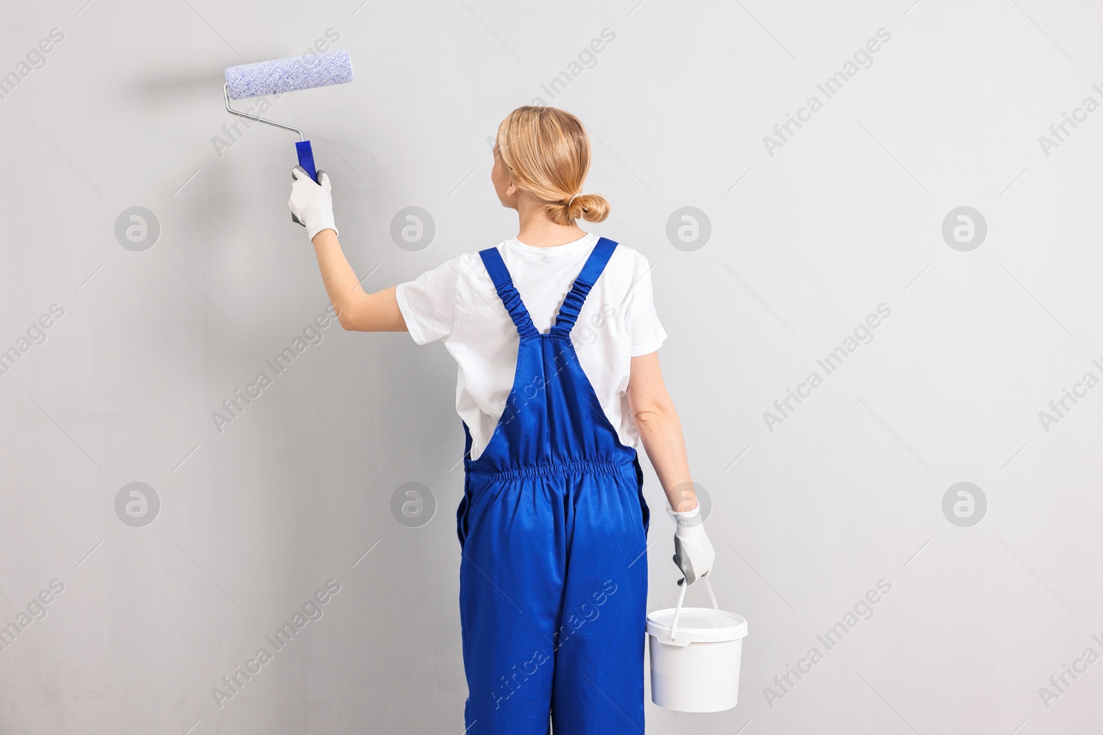 Photo of Female worker painting wall with roller indoors, back view