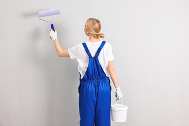 Female worker painting wall with roller indoors, back view