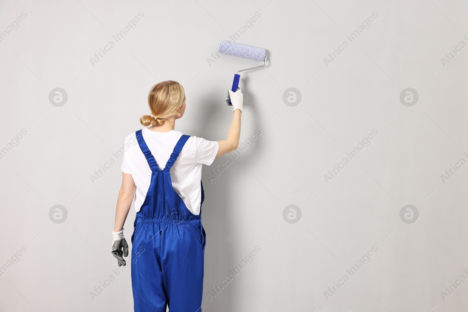 Photo of Female worker painting wall with roller indoors, back view. Space for text