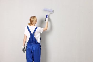 Female worker painting wall with roller indoors, back view. Space for text