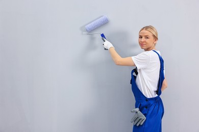 Photo of Female worker painting wall with roller indoors. Space for text