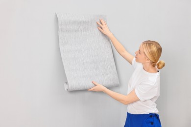 Female worker hanging grey wallpaper onto wall indoors. Space for text