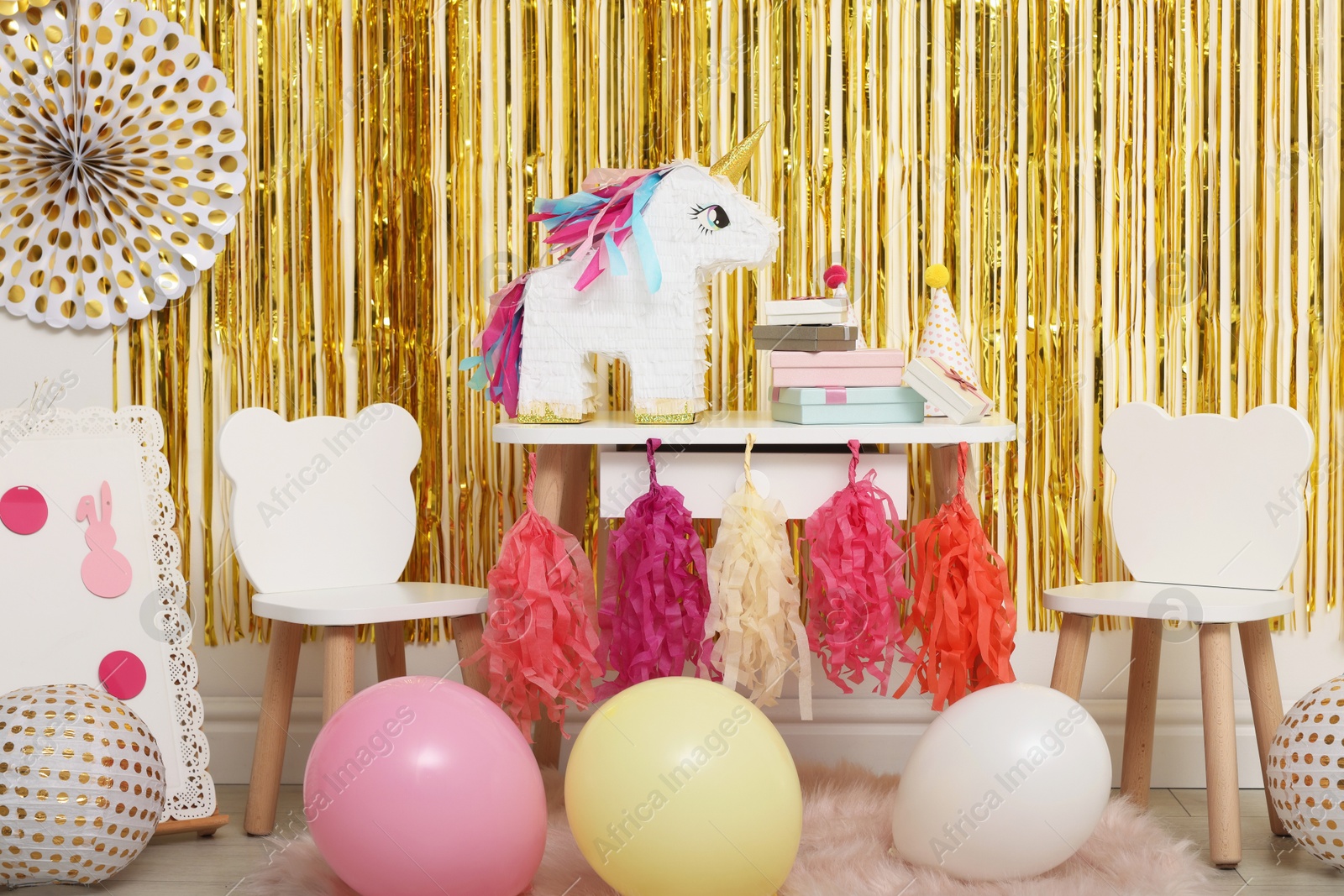 Photo of Bright pinata in shape of unicorn and party accessories against foil fringe curtain indoors