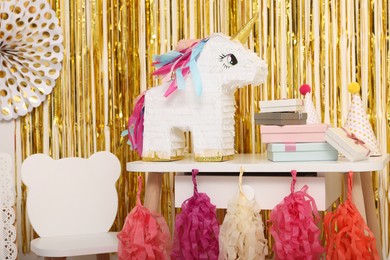 Photo of Bright pinata in shape of unicorn and party accessories against foil fringe curtain indoors