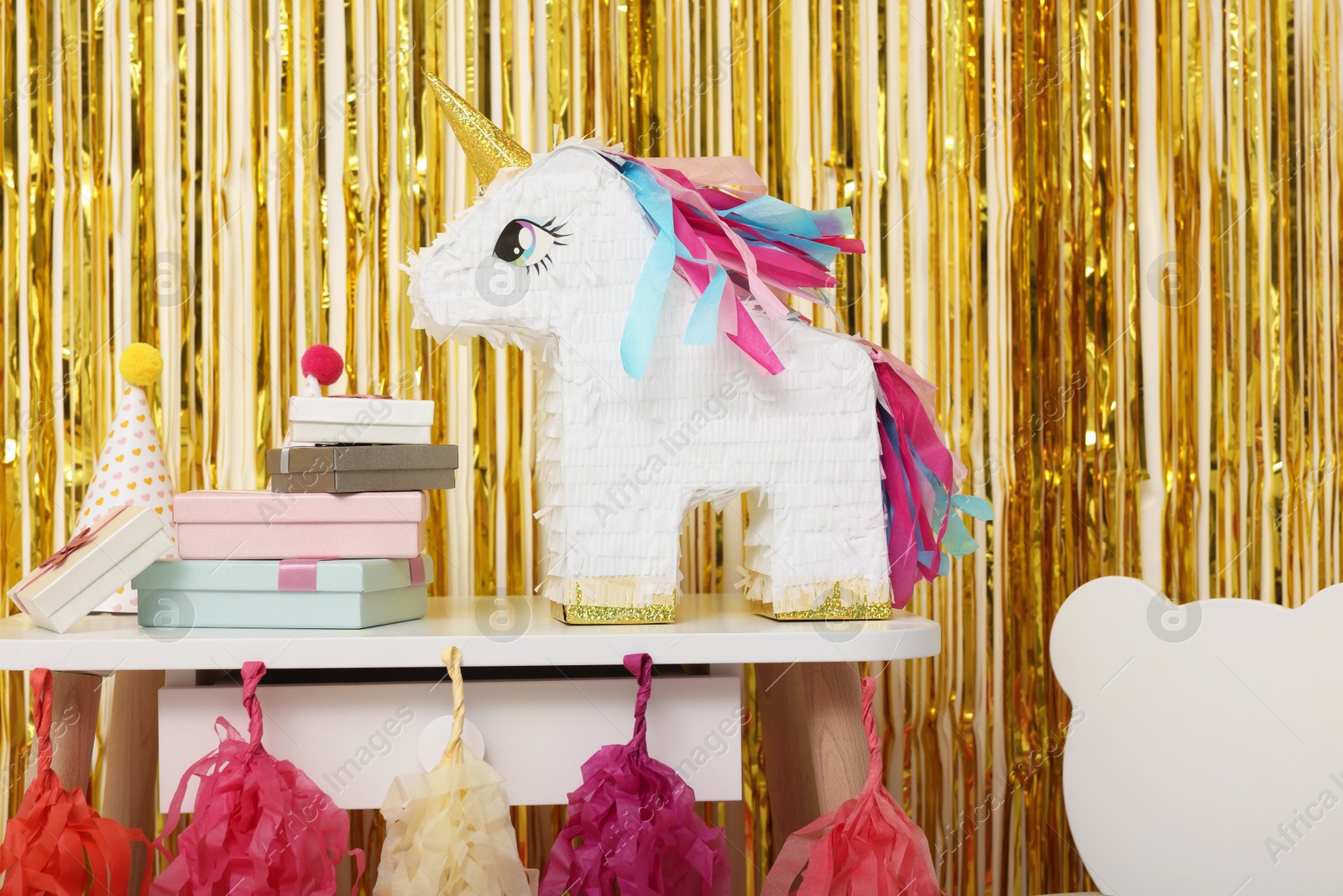 Photo of Bright pinata in shape of unicorn and party accessories against foil fringe curtain indoors