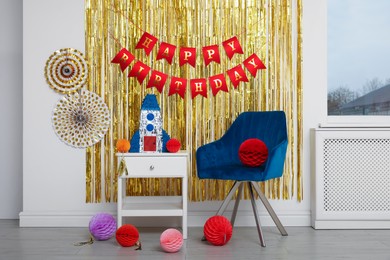 Photo of Bright pinata in shape of rocket and party accessories in festive decorated room