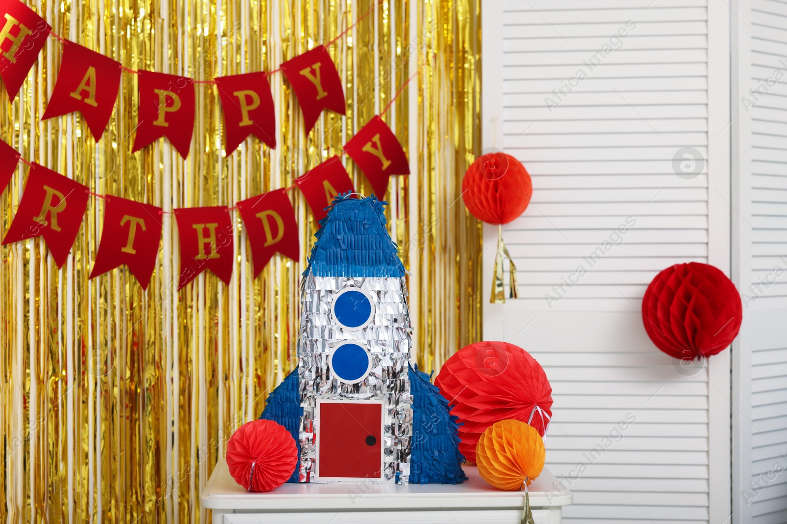 Photo of Bright pinata in shape of rocket and party accessories in festive decorated room