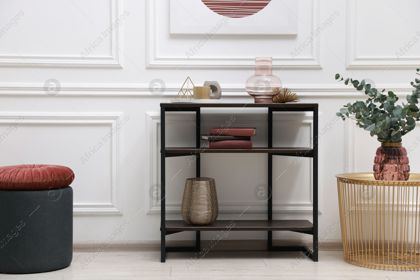 Photo of Console table with decor and pouf near white wall in room. Interior design