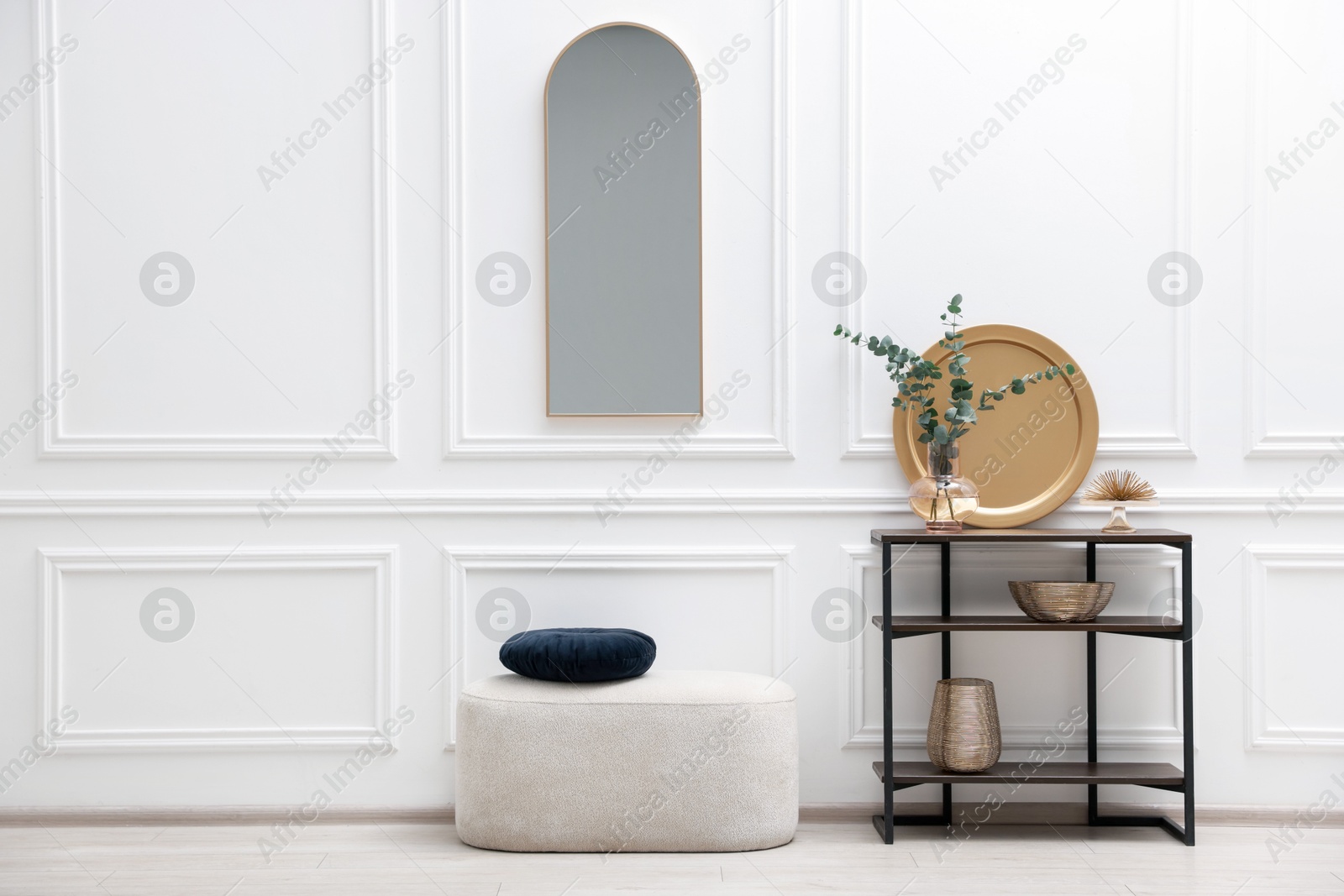 Photo of Console table with decor, pouf and mirror in room. Interior design