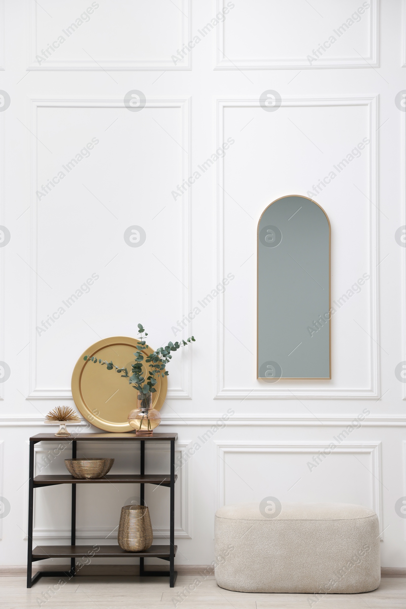 Photo of Console table with decor, pouf and mirror in room. Interior design