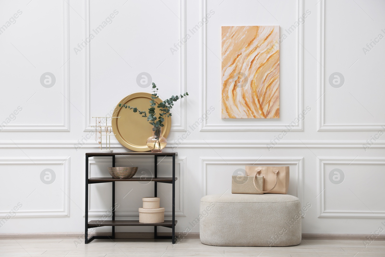 Photo of Console table with decor and pouf near white wall in room. Interior design