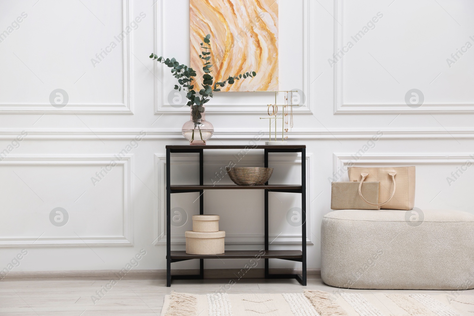 Photo of Console table with decor and pouf near white wall in room. Interior design