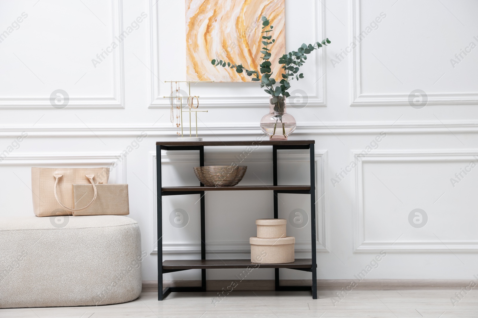 Photo of Console table with decor and pouf near white wall in room. Interior design