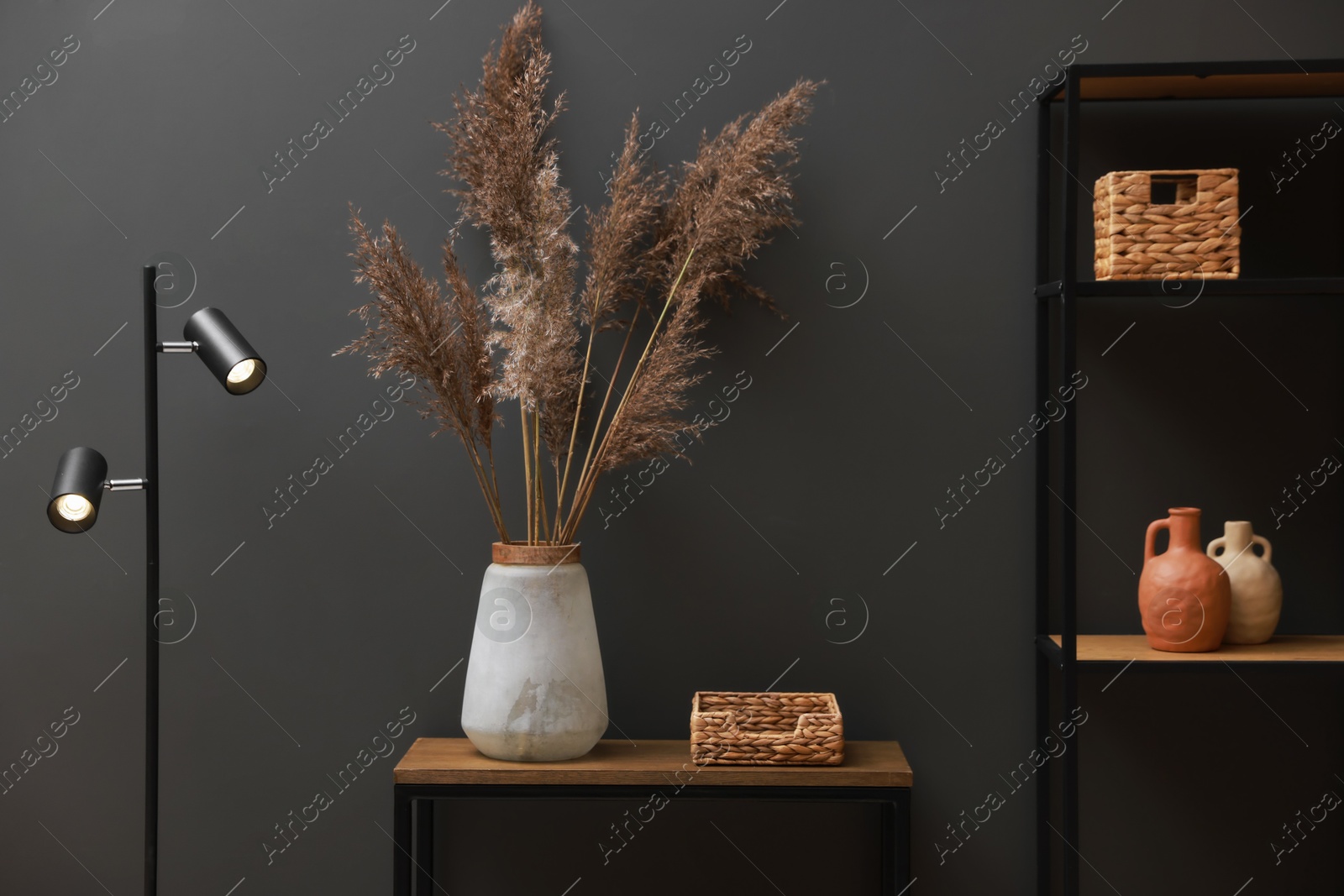 Photo of Console table with decor, lamp and shelving unit near grey wall in room. Interior design