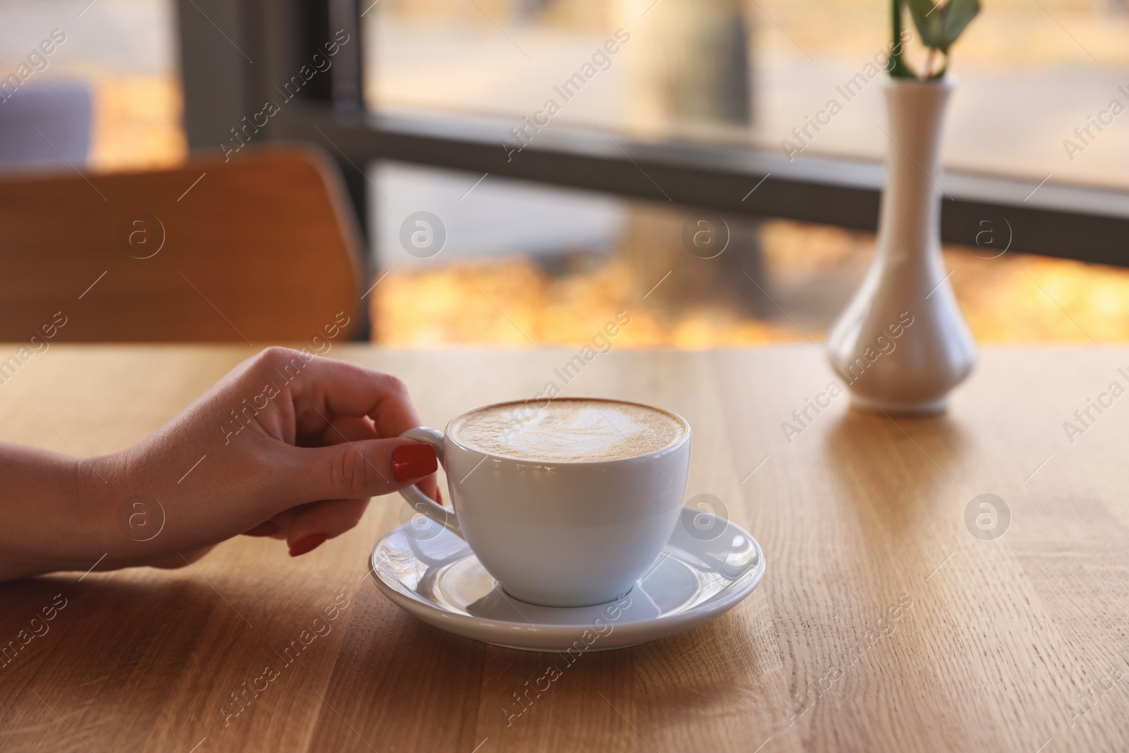 Photo of Woman with cup of aromatic coffee at wooden table in cafe, closeup