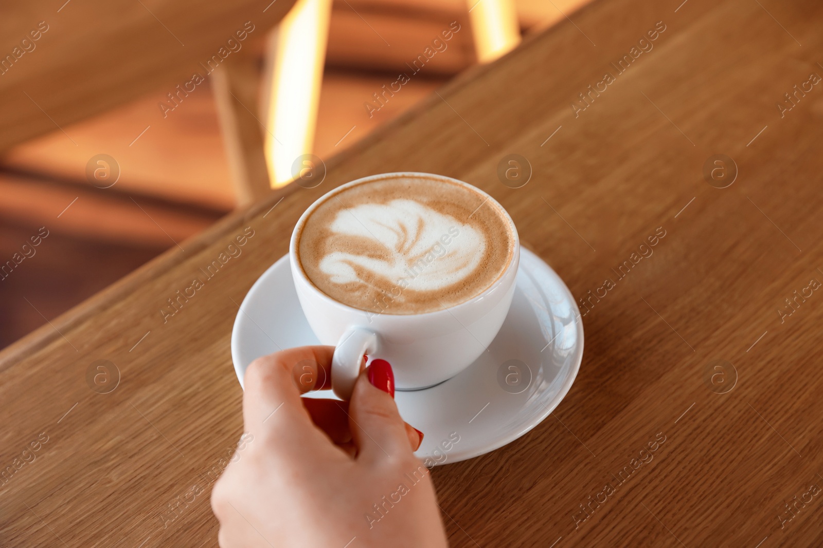 Photo of Woman with cup of aromatic coffee at wooden table in cafe, closeup