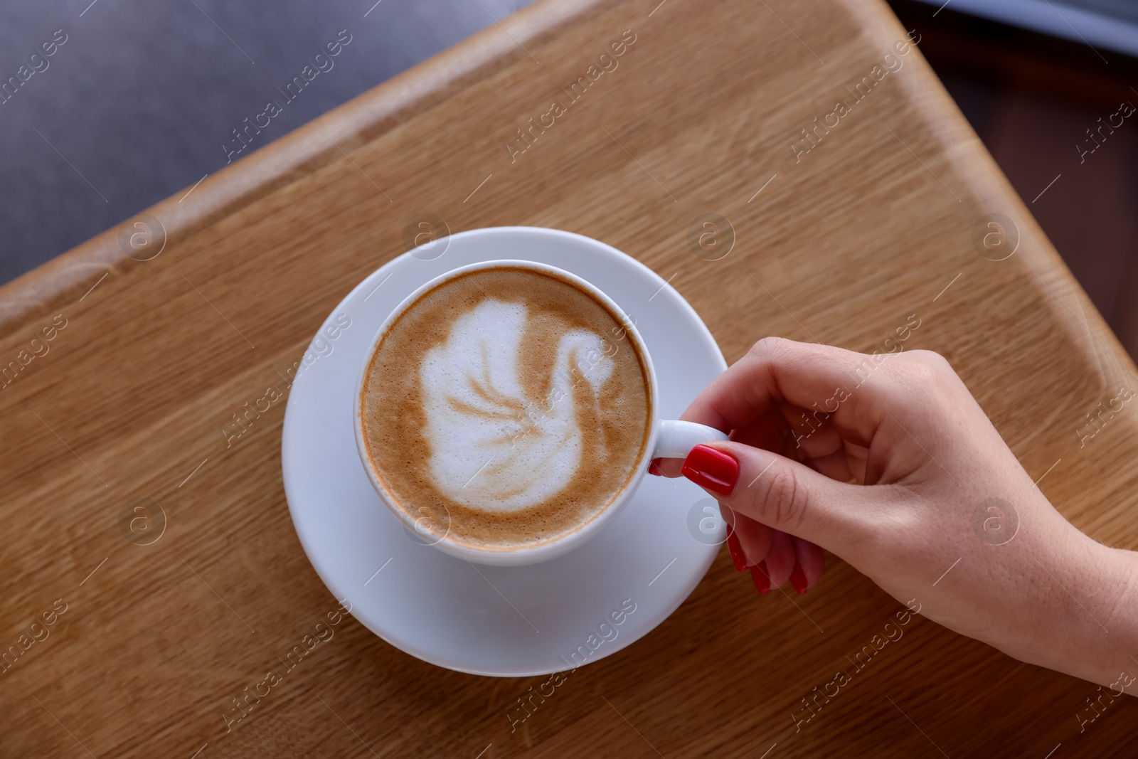 Photo of Woman with cup of aromatic coffee at wooden table in cafe, top view