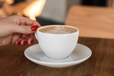 Photo of Woman with cup of aromatic coffee at wooden table in cafe, closeup