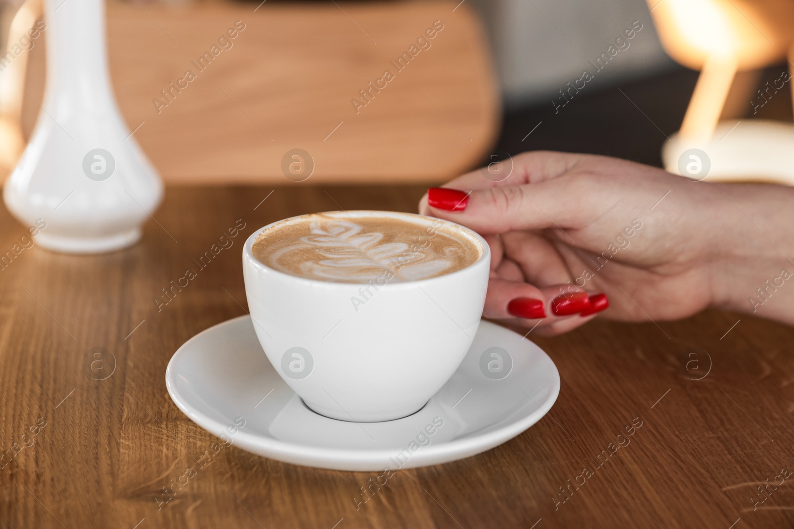 Photo of Woman with cup of aromatic coffee at wooden table in cafe, closeup