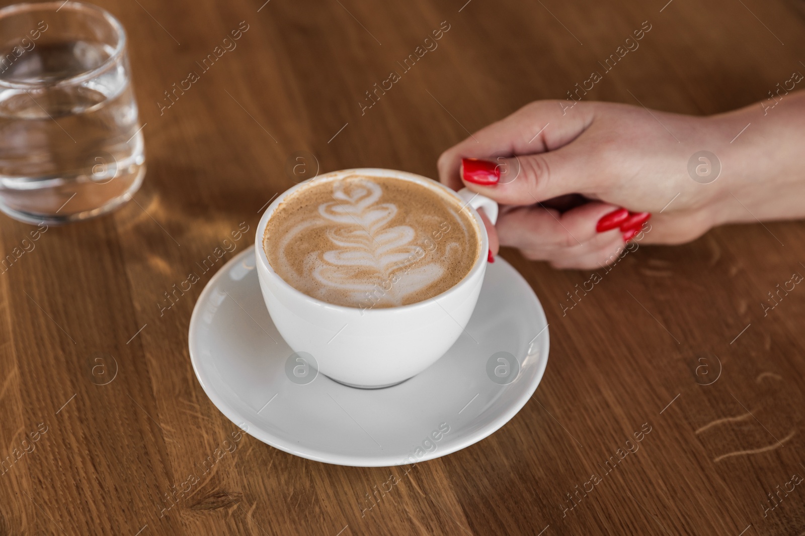 Photo of Woman with cup of aromatic coffee at wooden table in cafe, closeup