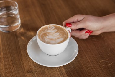 Photo of Woman with cup of aromatic coffee at wooden table in cafe, closeup