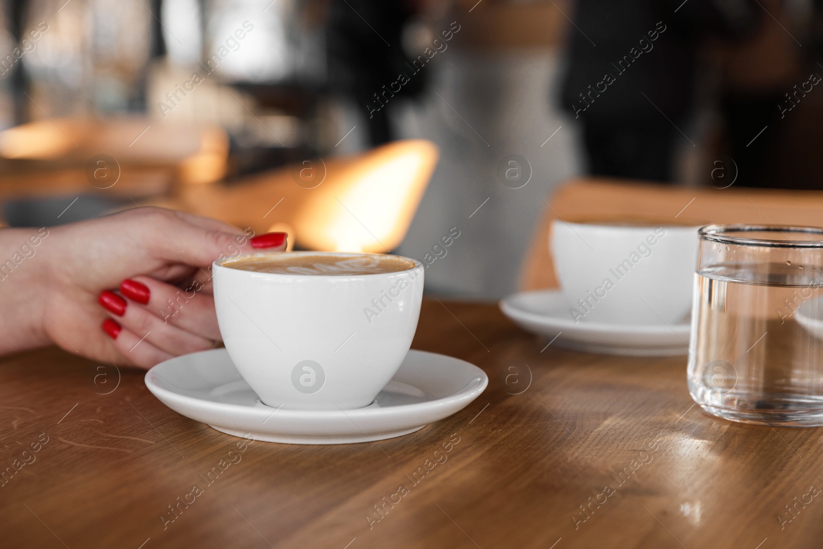 Photo of Woman with cup of aromatic coffee at wooden table in cafe, closeup