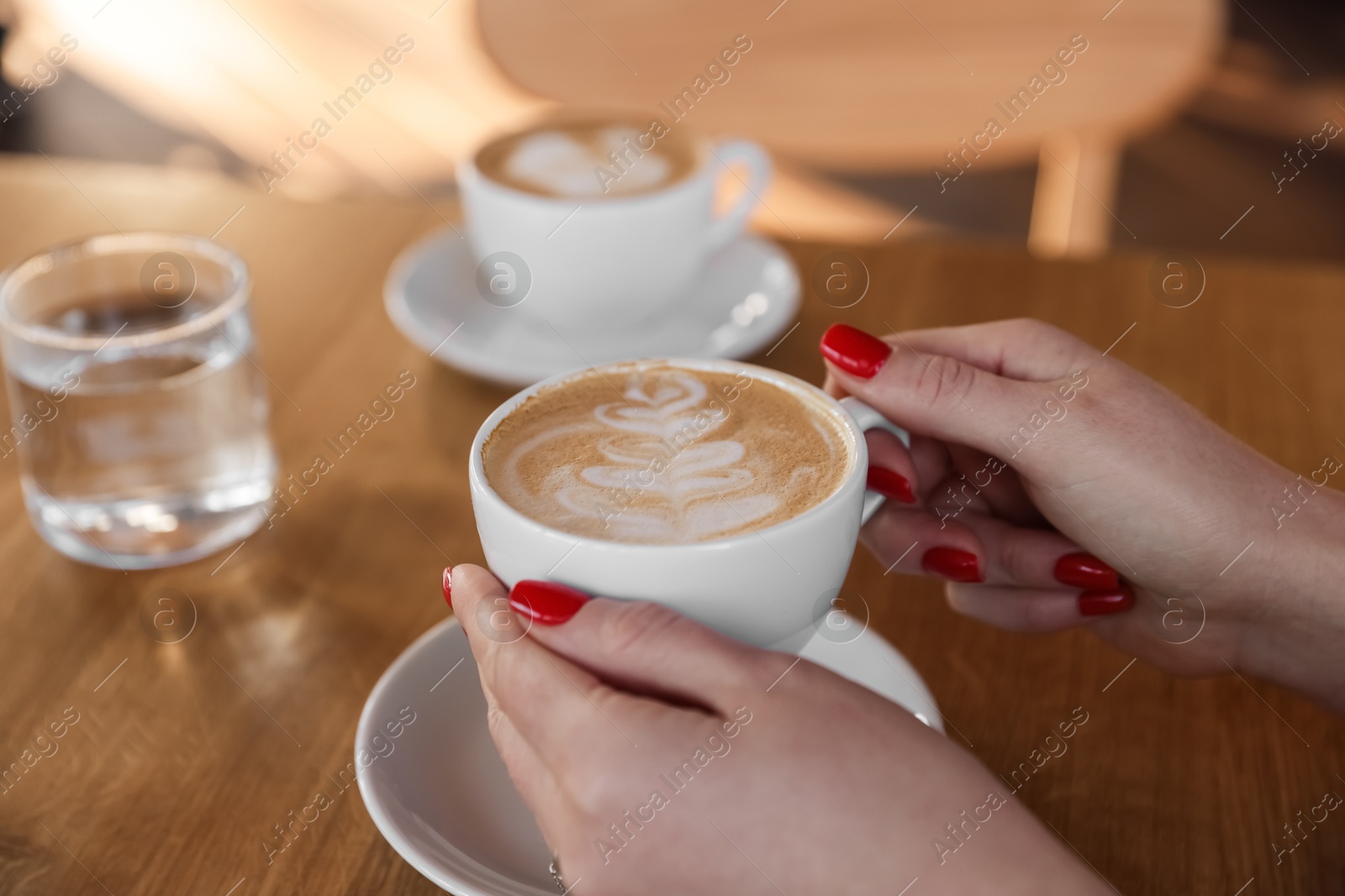 Photo of Woman with cup of aromatic coffee at wooden table in cafe, closeup