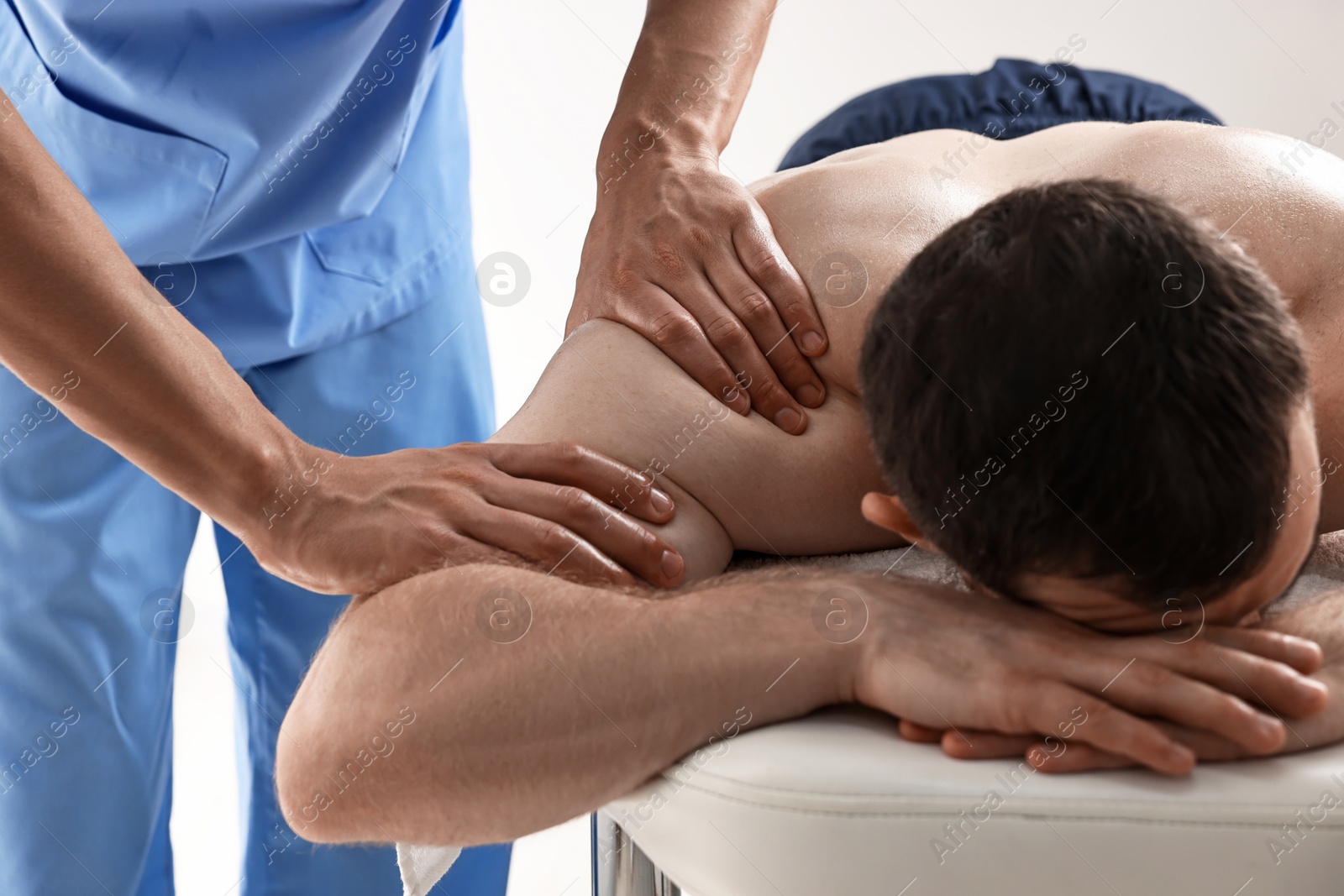 Photo of Professional physiotherapist doing shoulder massage for his client indoors, closeup