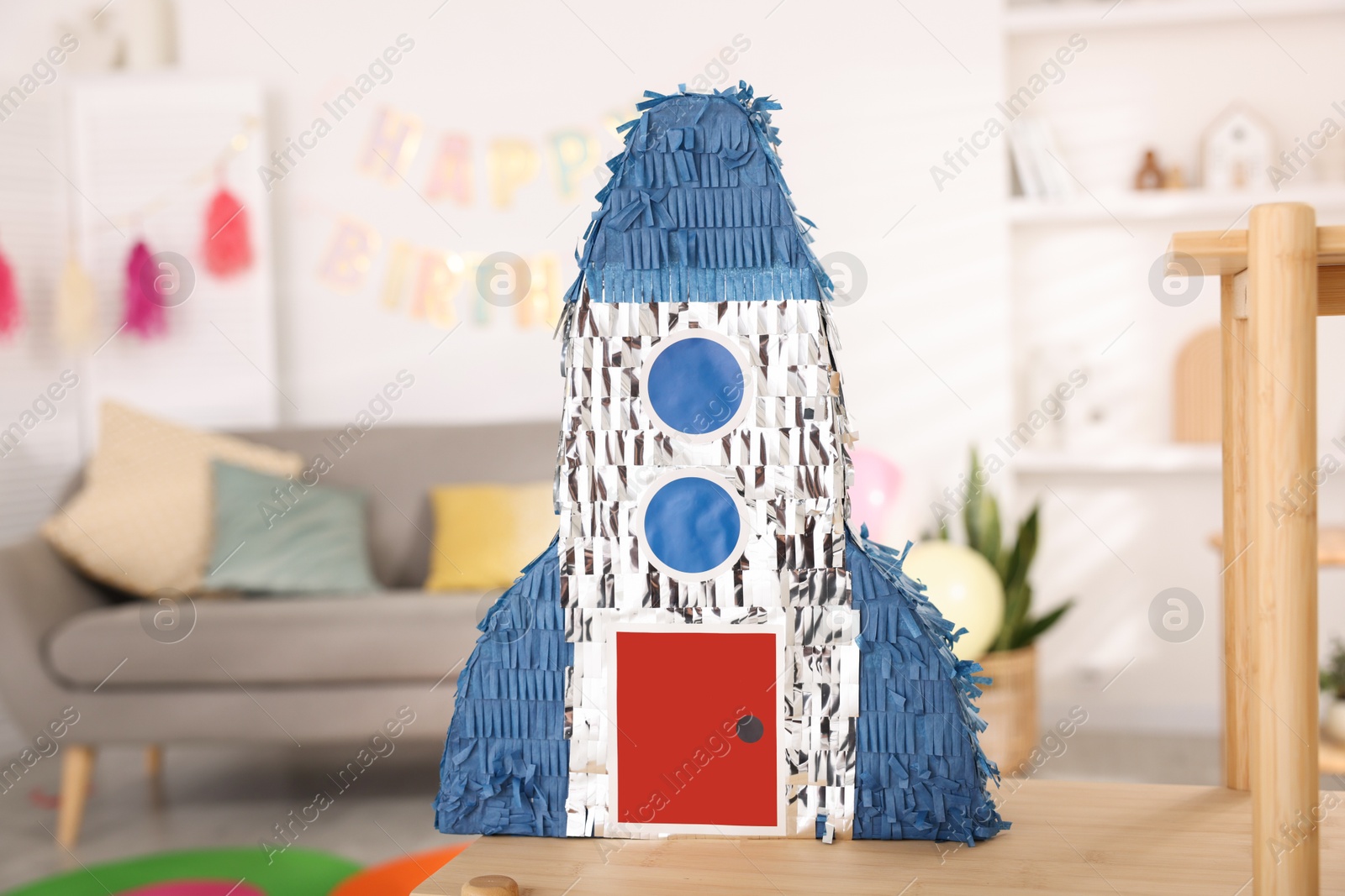 Photo of Bright pinata in shape of rocket on wooden table in festive decorated room