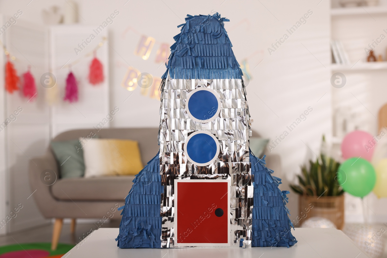 Photo of Bright pinata in shape of rocket on table in festive decorated room