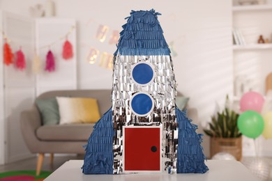 Photo of Bright pinata in shape of rocket on table in festive decorated room