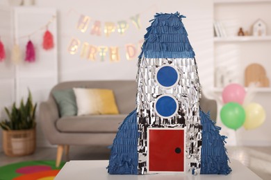 Photo of Bright pinata in shape of rocket on table in festive decorated room, space for text